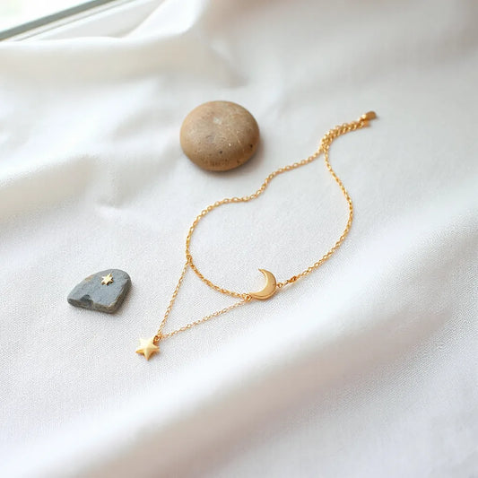 Minimal crescent moon and star charm necklace with matching bracelet on a light fabric background