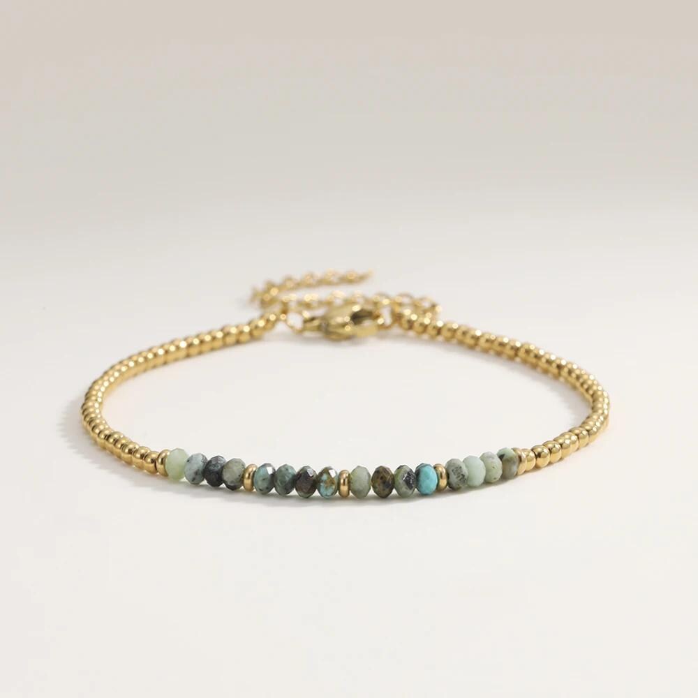 Gold bracelet with small beads on a light gray background