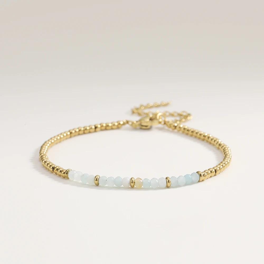 Gold bracelet with white beads on a light gray background