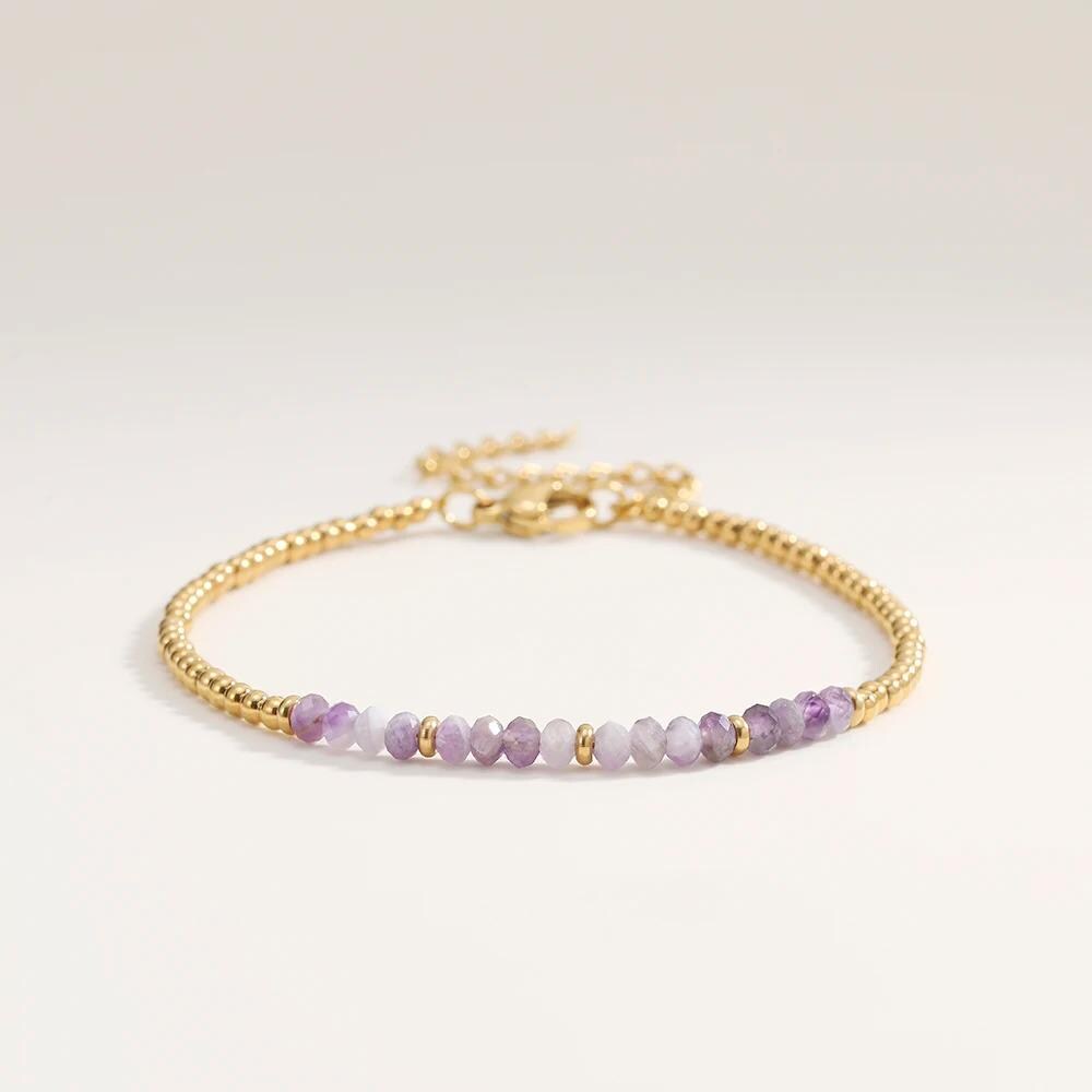 Gold bracelet with purple beads on a light gray background