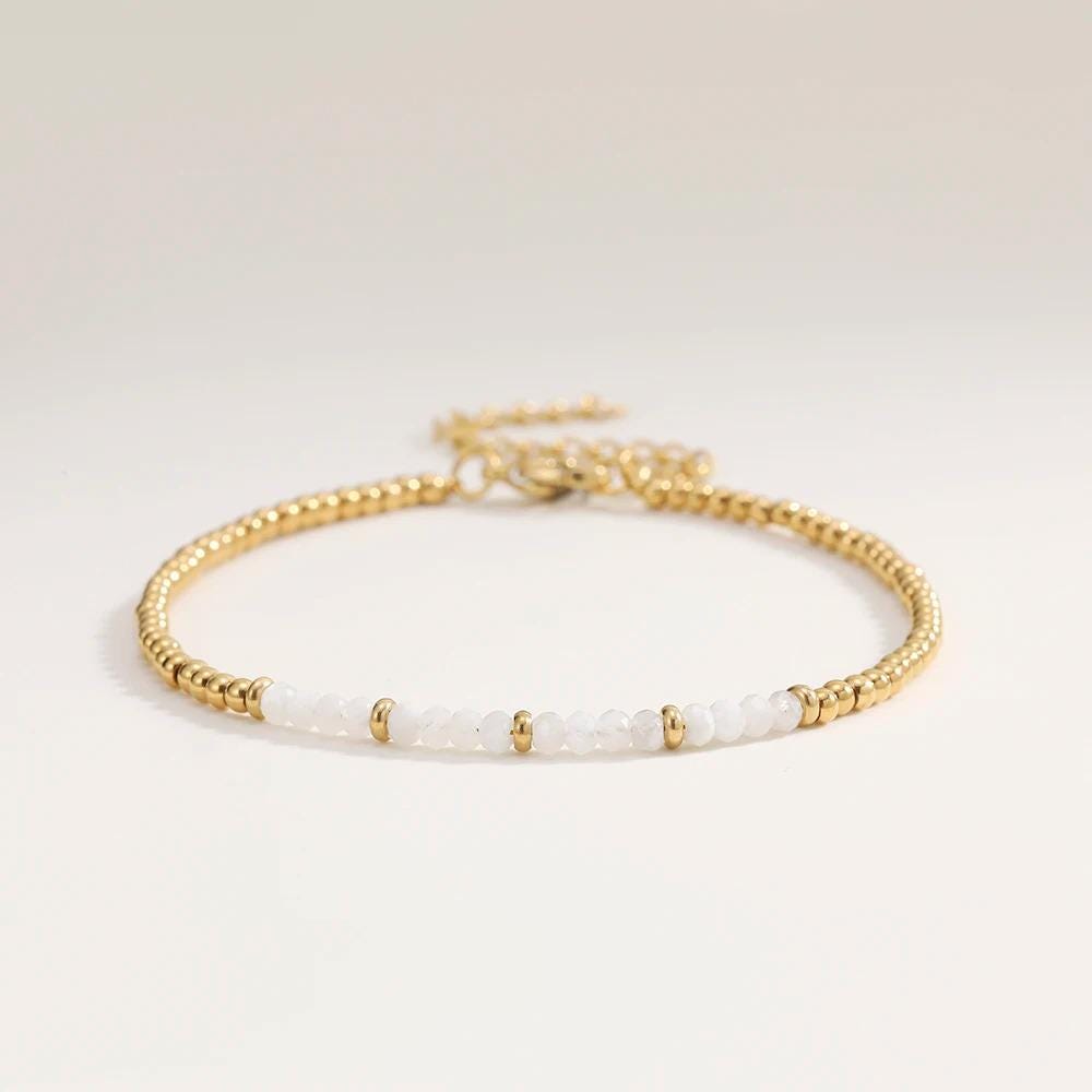 Gold bracelet with white beads on a light gray background