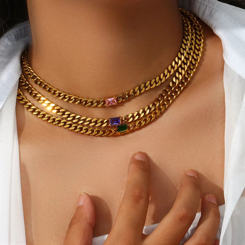 Gold chain necklace with colorful gemstones worn by a person against a white background