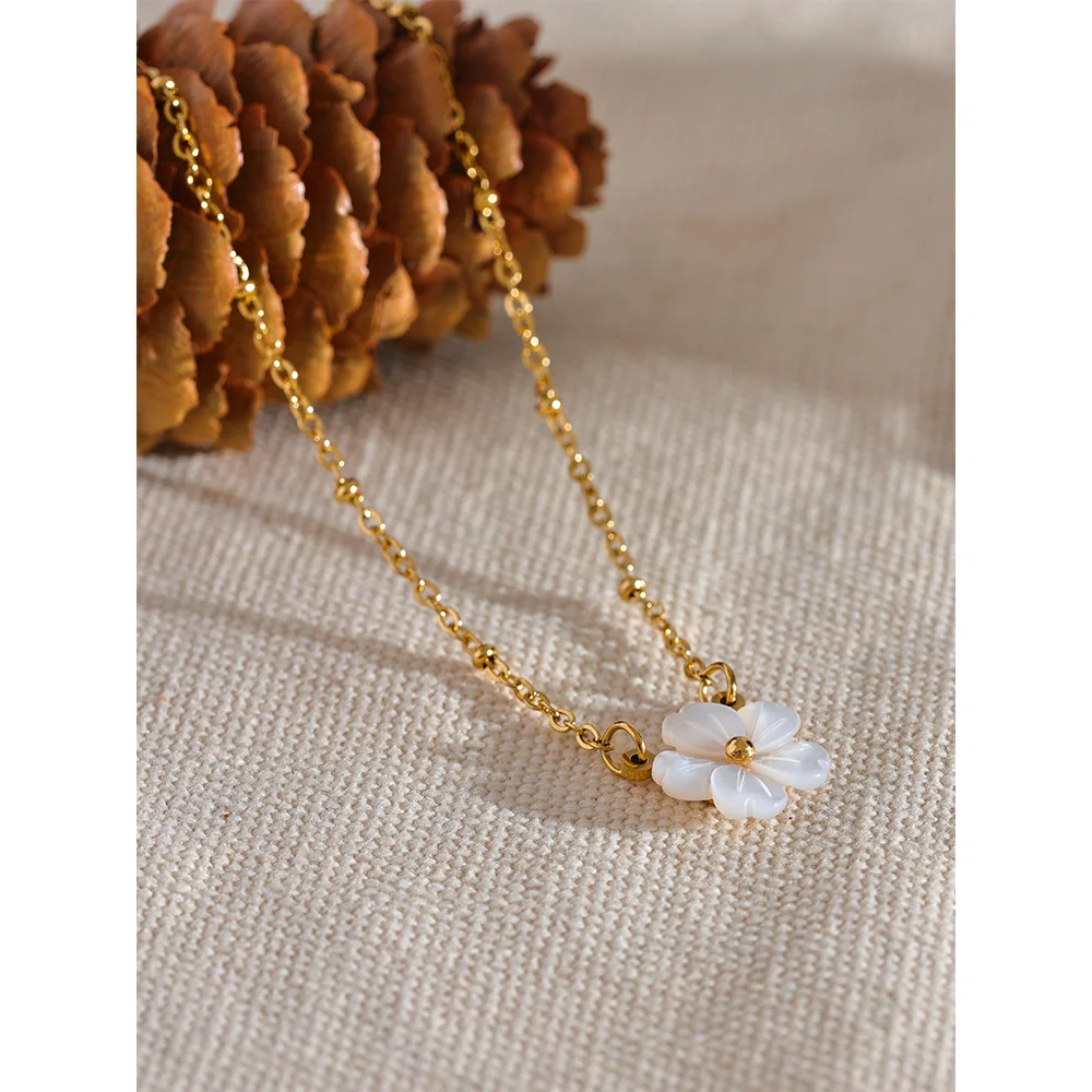 Gold necklace with a white flower pendant on a textured surface