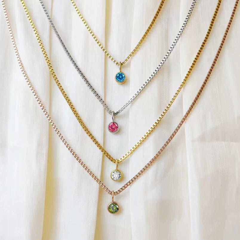 Three necklaces with colorful gemstones on a white fabric background, branded 'Mango Stainless Steel Jewelry'.