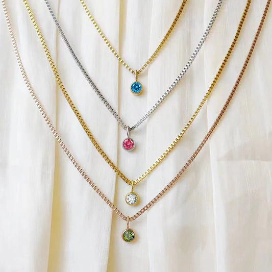 Three necklaces with colorful gemstones on a white fabric background, branded 'Mango Stainless Steel Jewelry'.