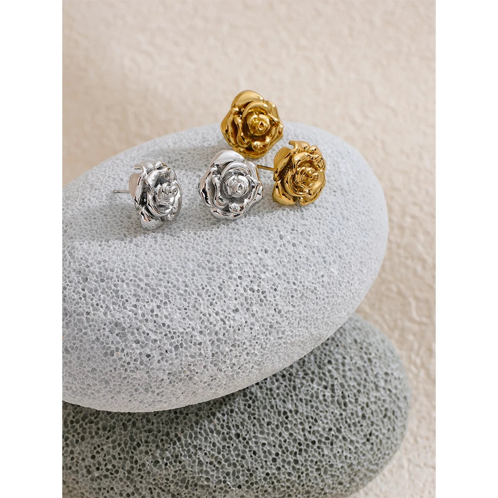 Gold and silver rose-shaped earrings on a textured stone surface