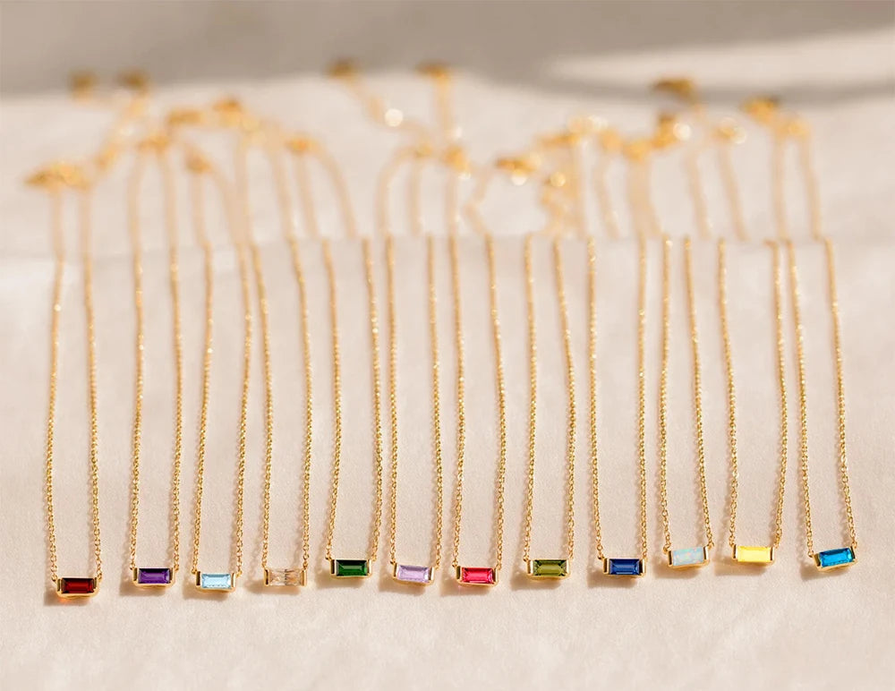 Gold necklaces with colorful gemstones on a white surface, branded 'Manco Stainless Steel Jewelry'.