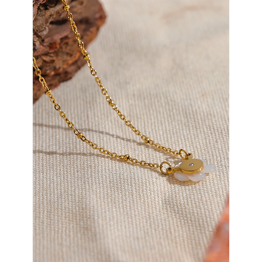 Gold necklace with a small pendant on a textured beige surface