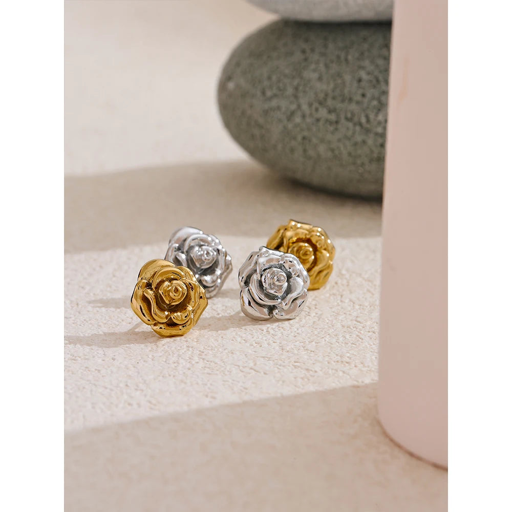 Three rose-shaped earrings in gold, silver, and bronze on a textured surface.