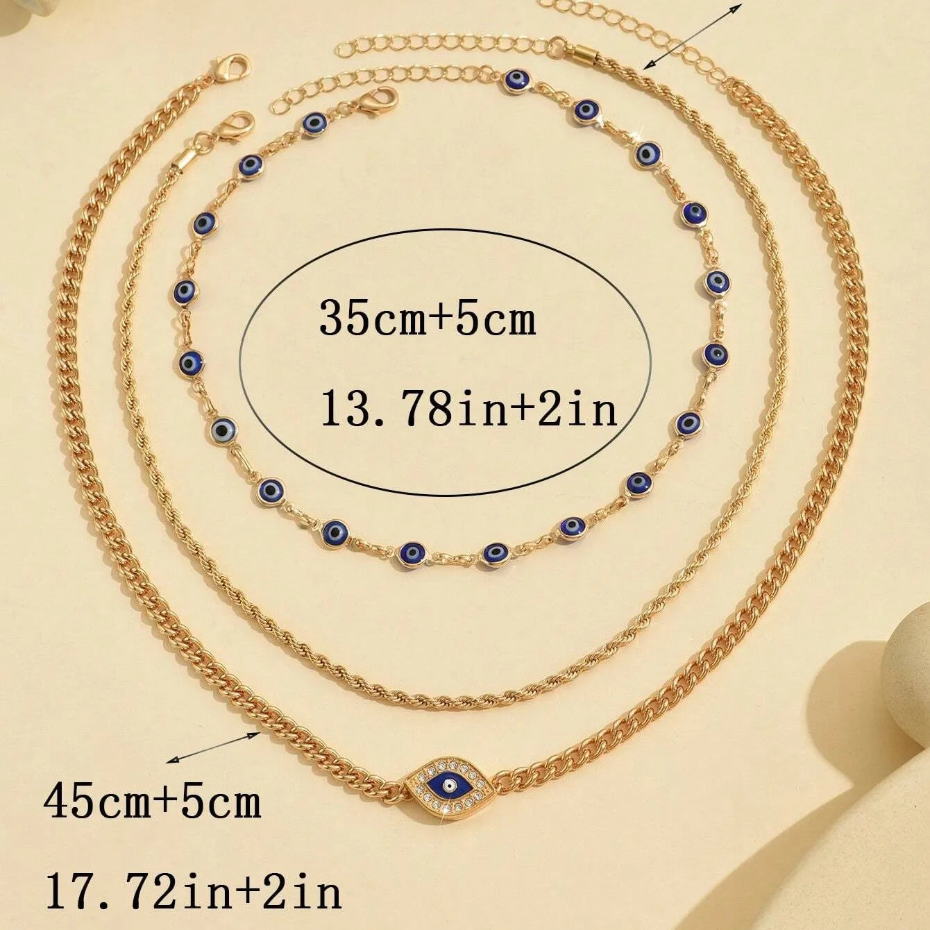 Gold necklaces with blue evil eye charms on a beige background