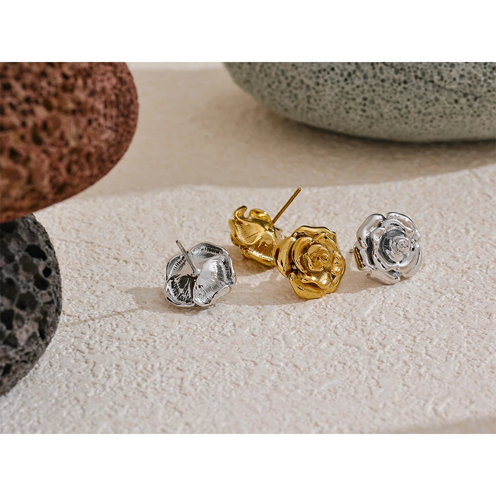 Three pairs of rose-shaped earrings in gold and silver on a textured surface.