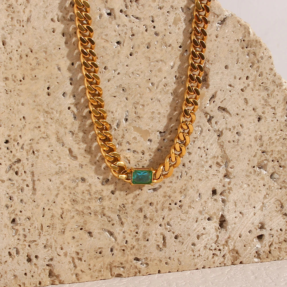 Gold chain necklace with a green stone on a textured beige background