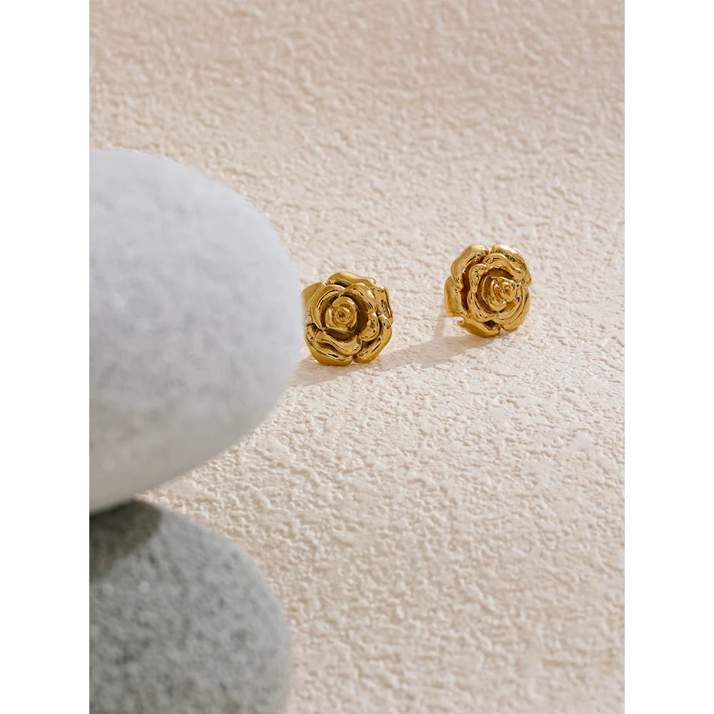 Gold rose-shaped earrings on a textured beige surface