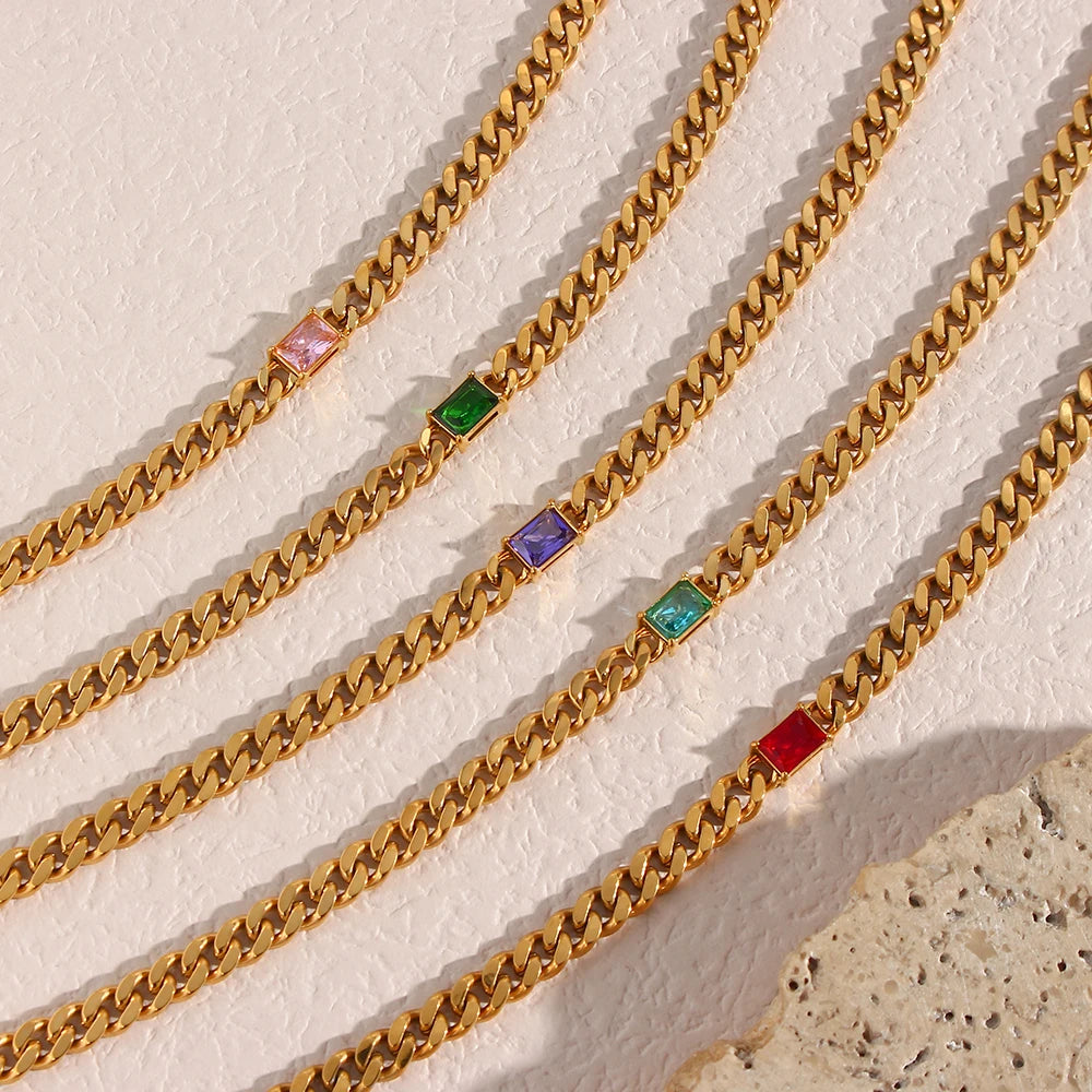 Gold chain with colorful square beads on a textured beige surface